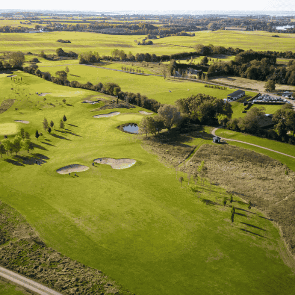 Luftfoto af golfbane med træer, stier og bunkers. 