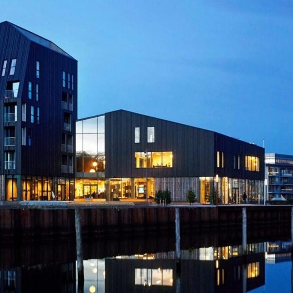 En klynge af blandede bygninger nede ved en havnefront om aftenen med tændte lys