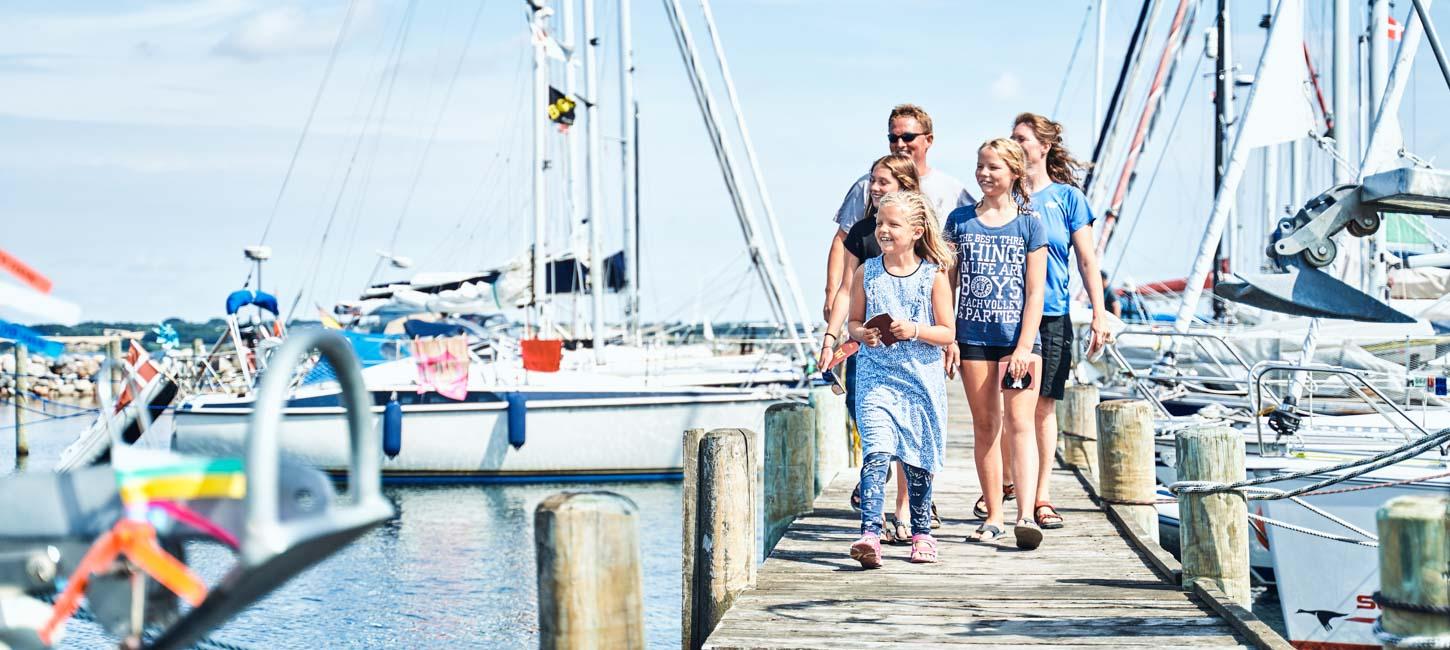 En familie kommer gående på en havn med en masse skibe i baggrunden.