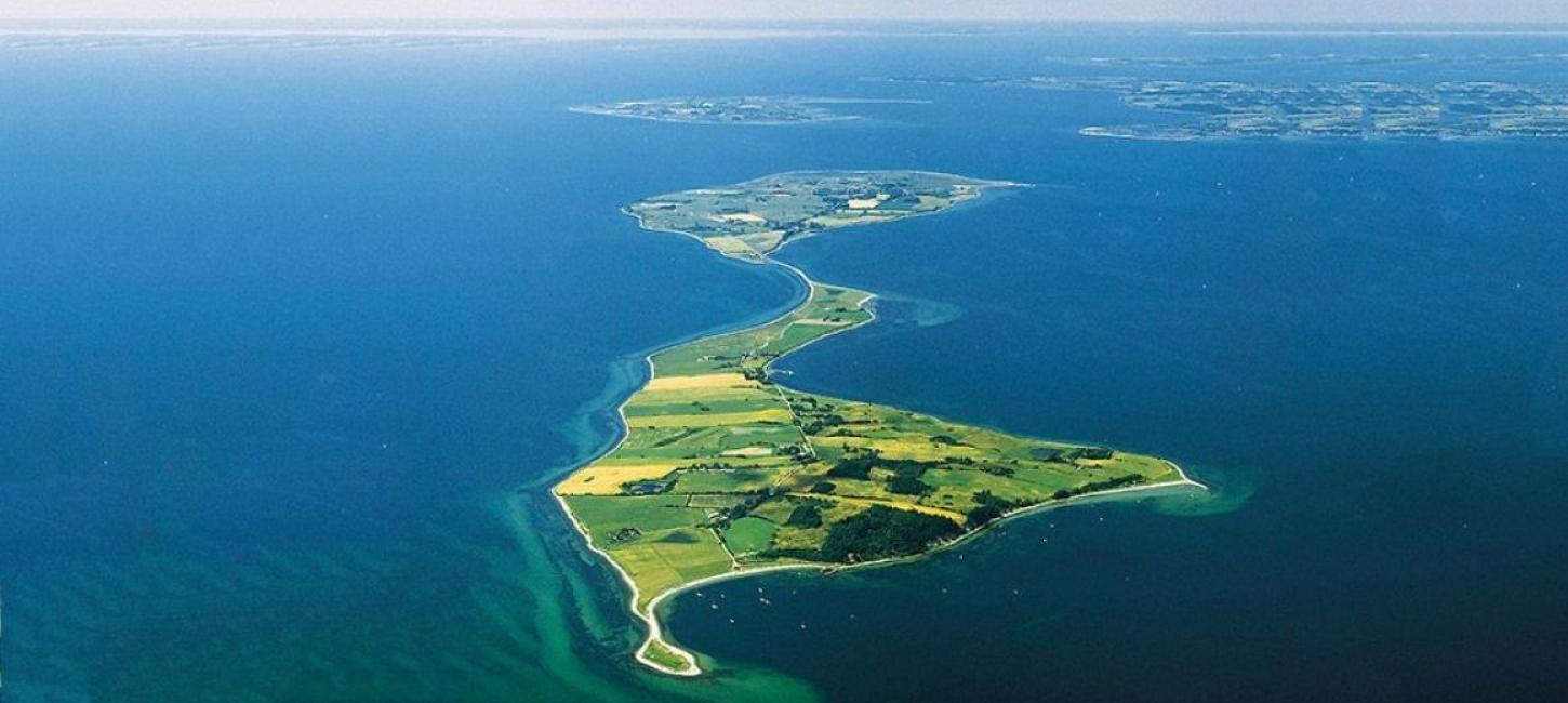 Dronephoto of Avernakø i sharp, lush, green colors with oceanblue water all around the shores