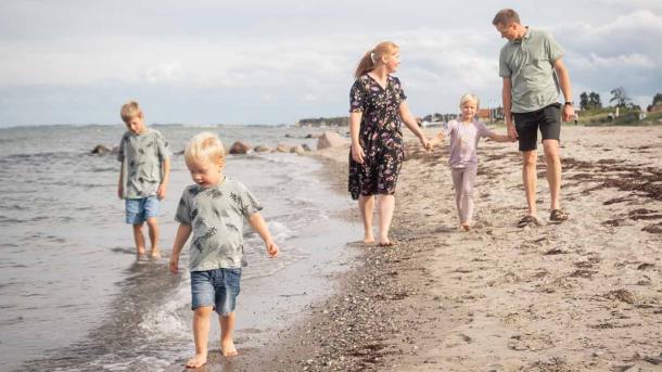 En familie med mor, far, og tre børn, går langs vandkanten på en strand på Nordfyn