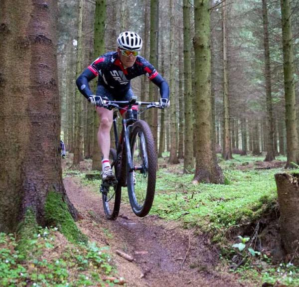 En mountainbiker i skoven, omringet af træer og vildt mos.