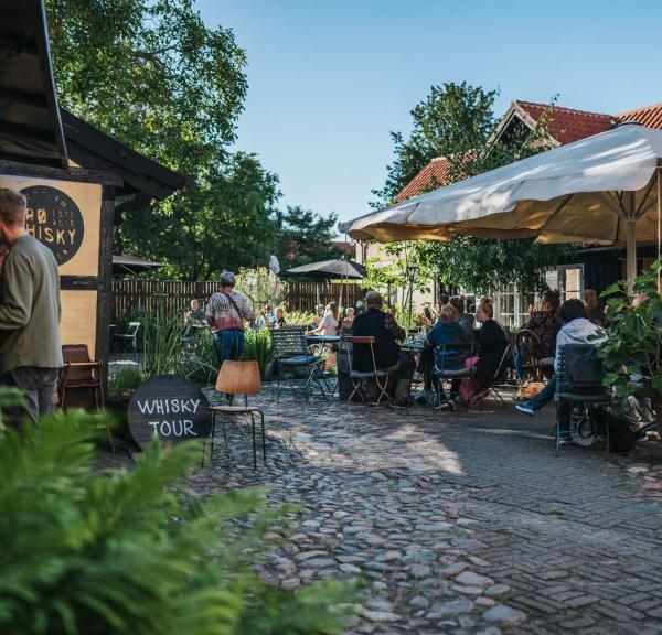 En brostensbelagt gårdhave med servering, parasol og store plantekrukker