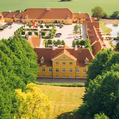 Et dronebillede af Broløkke Herregård med grønne marker og skov