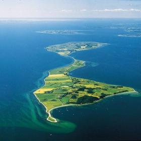 Dronephoto of Avernakø i sharp, lush, green colors with oceanblue water all around the shores