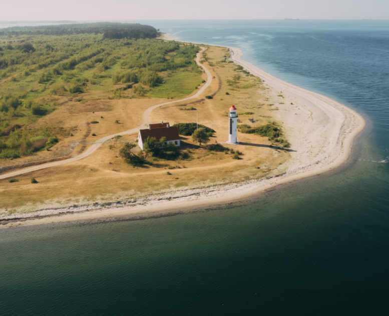 Et dronefoto af en kyst med et fyrtårn og blå hav